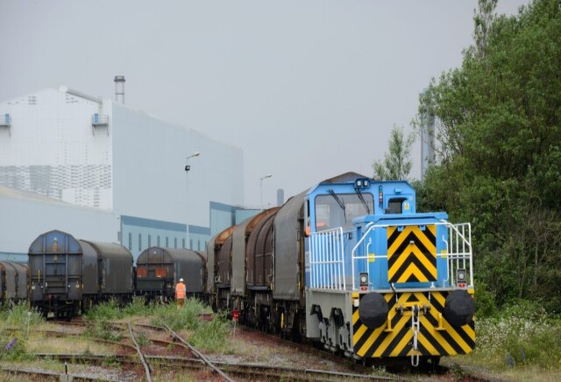 Electric-converted locomotive hauling freight wagons through an industrial rail yard, highlighting the long-term value and sustainability of transitioning from diesel to electric propulsion.